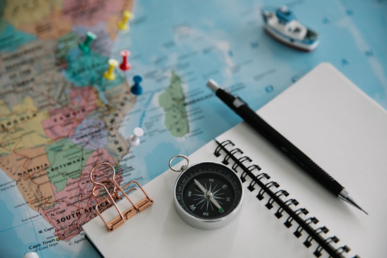 heros-img Flat lay of travel planning tools including a map, compass, notebook, and pen.